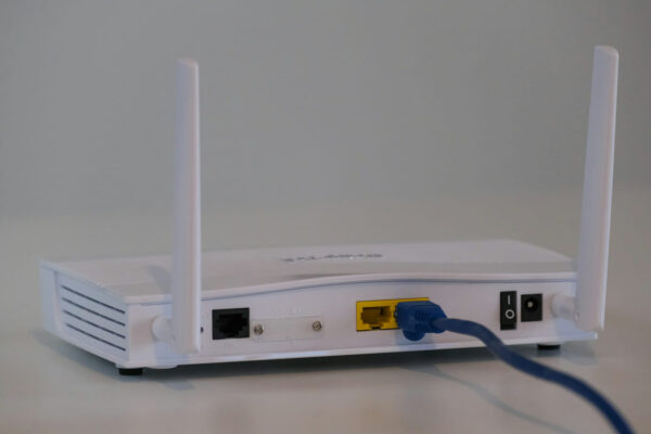 Rückseite eines weißen Routers mit angeschlossenen Kabeln und sichtbaren Anschlüssen